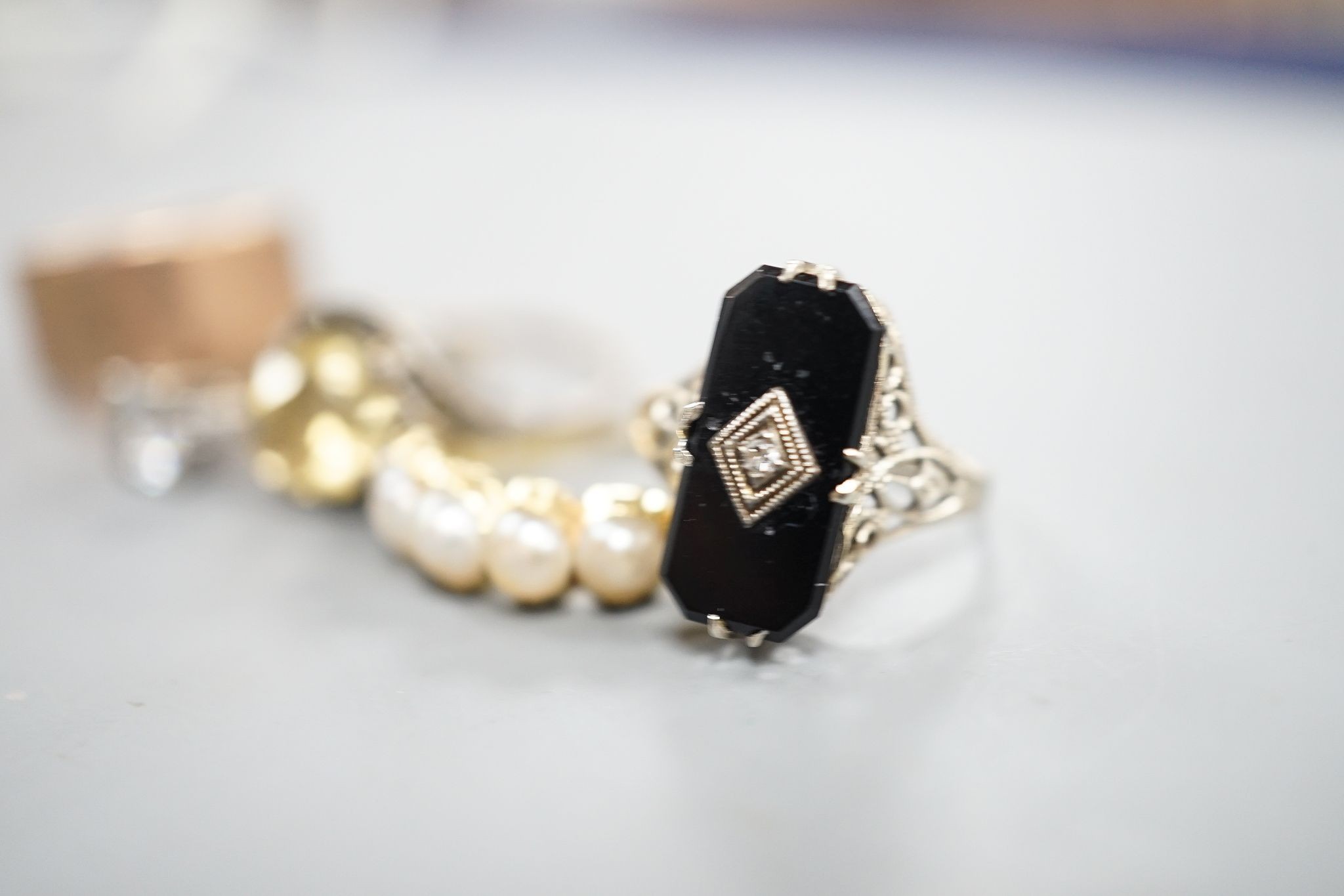 A 9ct gold wedding band, 4.8 grams, a yellow metal and split pearl set half hoop ring, a black onyx and diamond chip set ring, a 9ct and paste ring and one other ring.